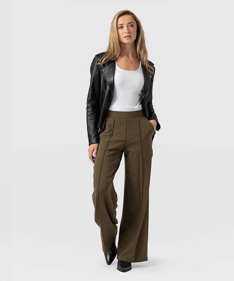 A model wearing wide leg trousers with an elasticated waistband and pressed centre creases. Worn with a white tank top and black leather jacket.