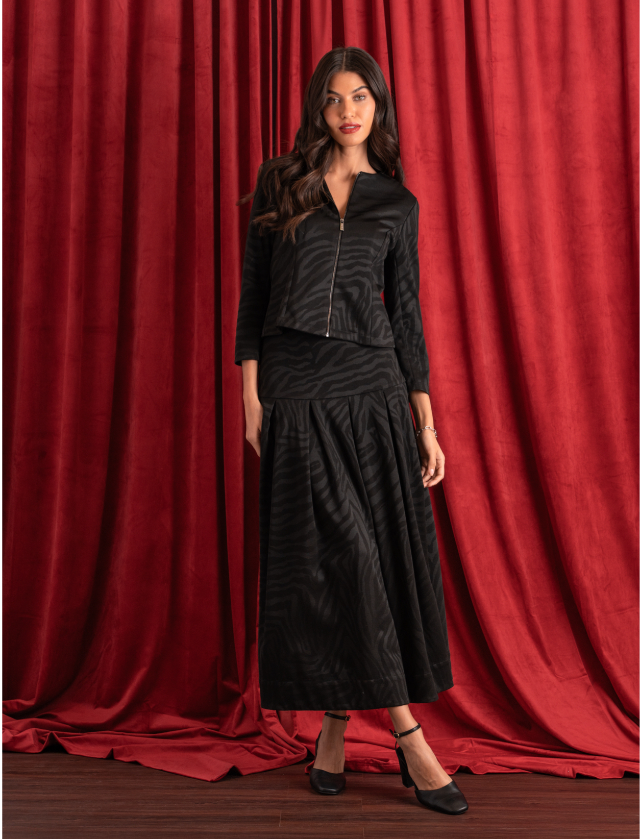 Woman wearing a pleated midi skirt in black zebra print with a matching jacket in black zebra print