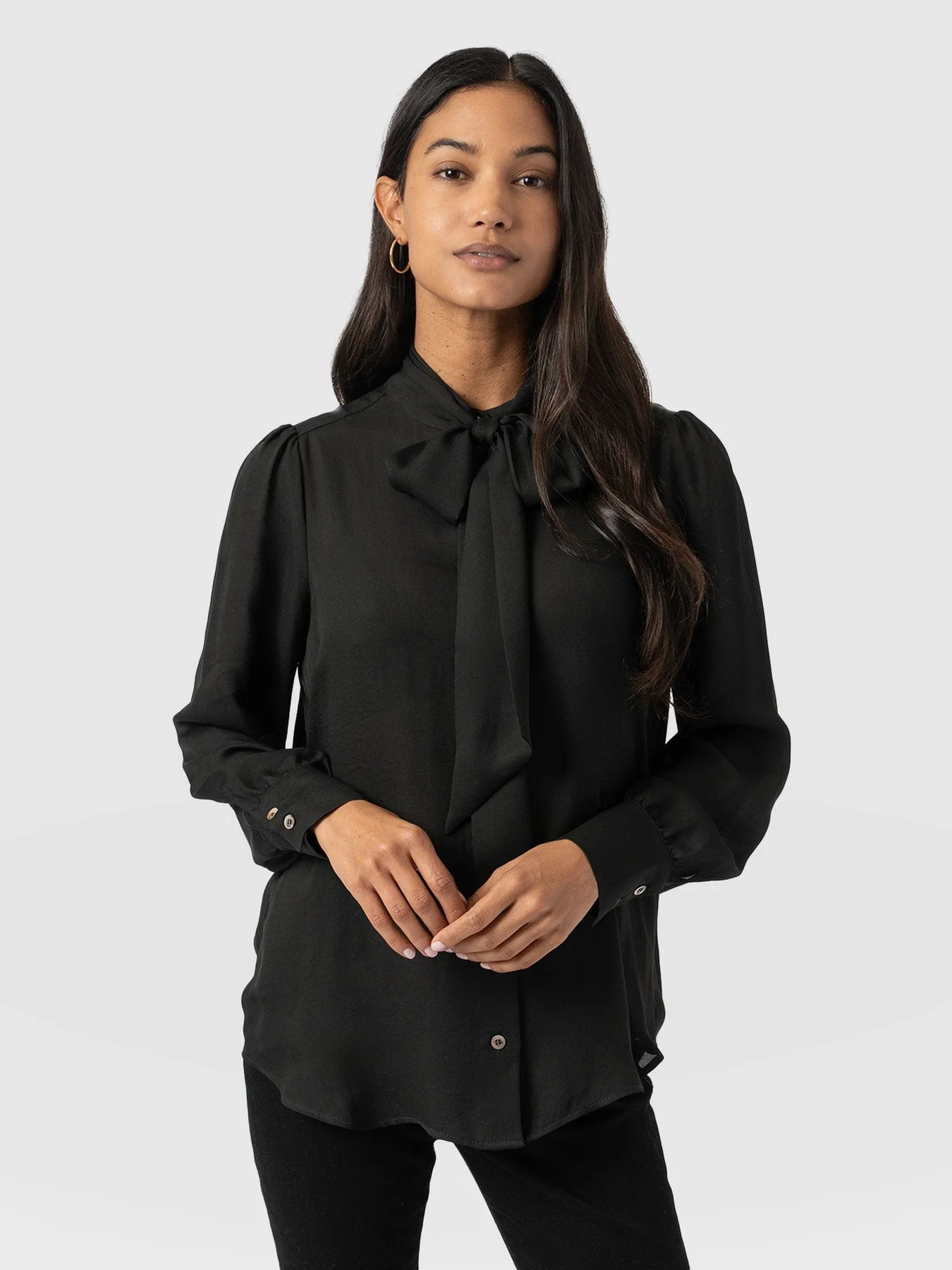 A model wearing a black blouse with a pussybow neckline from the Saint and Sofia November collection.