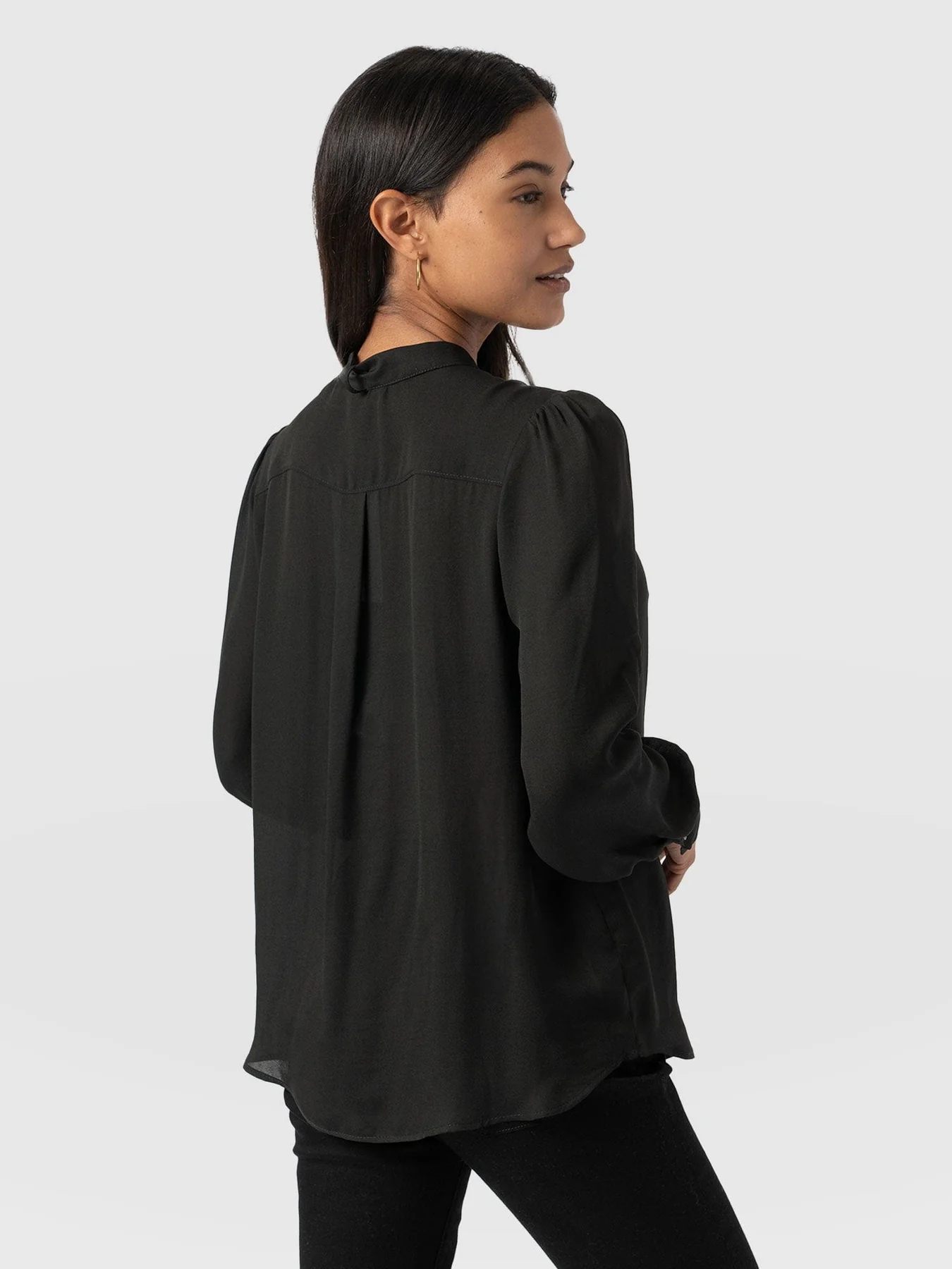 A model turned to the back wearing a black semi-sheer blouse from the Saint and Sofia November collection.
