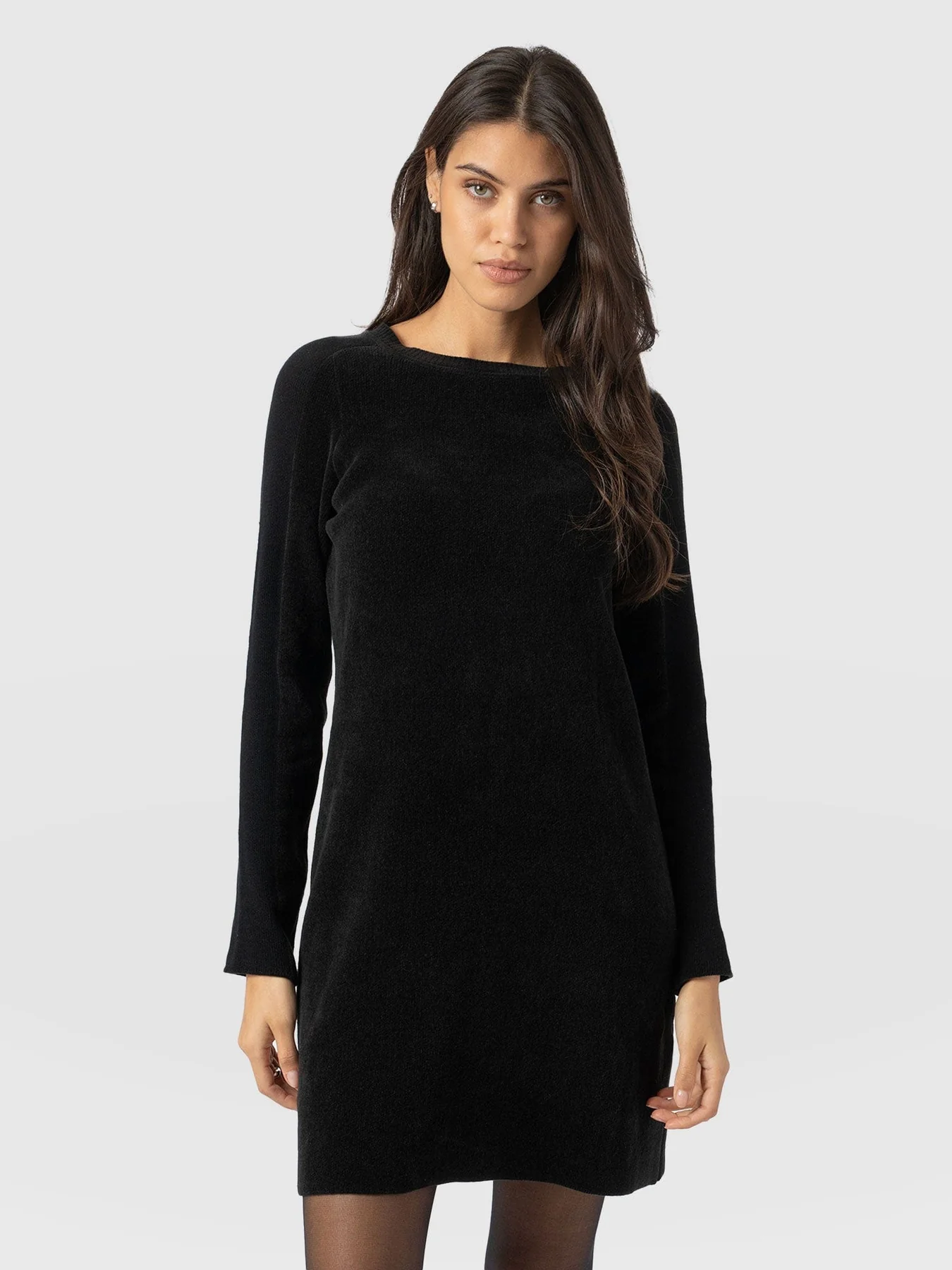 A model wearing the Saint and Sofia Raya Knit dress. A long sleeve black knitted dress with a crew neckline and mini-length skirt.
