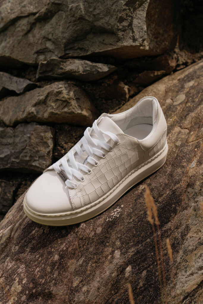 A white leather trainer with a croc-embossed detail and a Saint and Sofia brand plaque at the front lace.