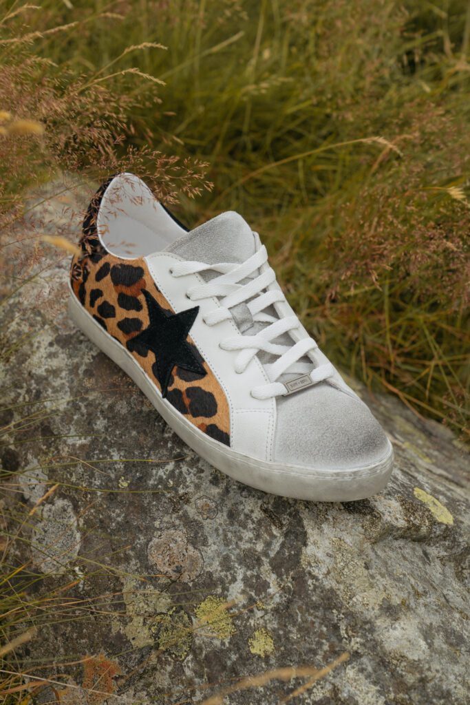 A suede leopard print trainer with a black star patch at the side and a white leather toe cap.