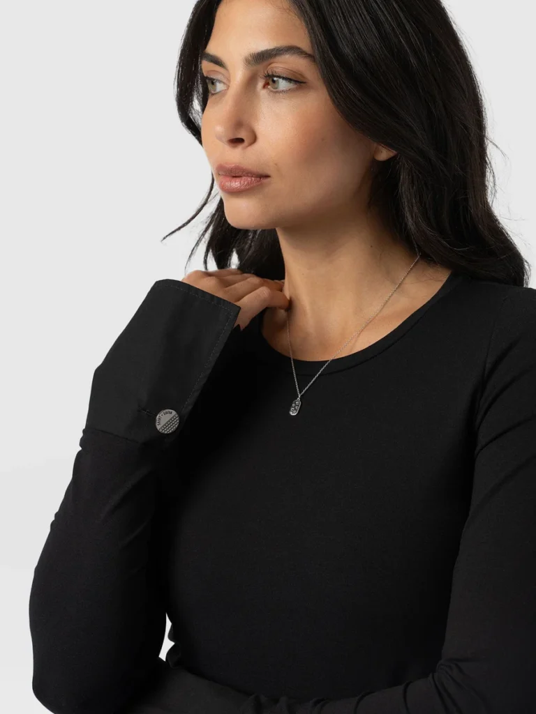 A model wearing the Saint and Sofia Connie Cuff tee in black. A long-sleeved, slim-fitting top with a crew neckline and shirt-style buttoned cuffs.