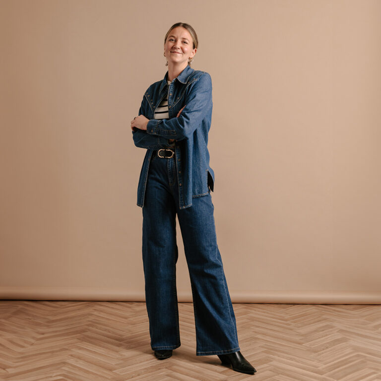 The Saint and Sofia Senior Designer, Danielle. Stood in front of a beige background wearing a double-denim suit.