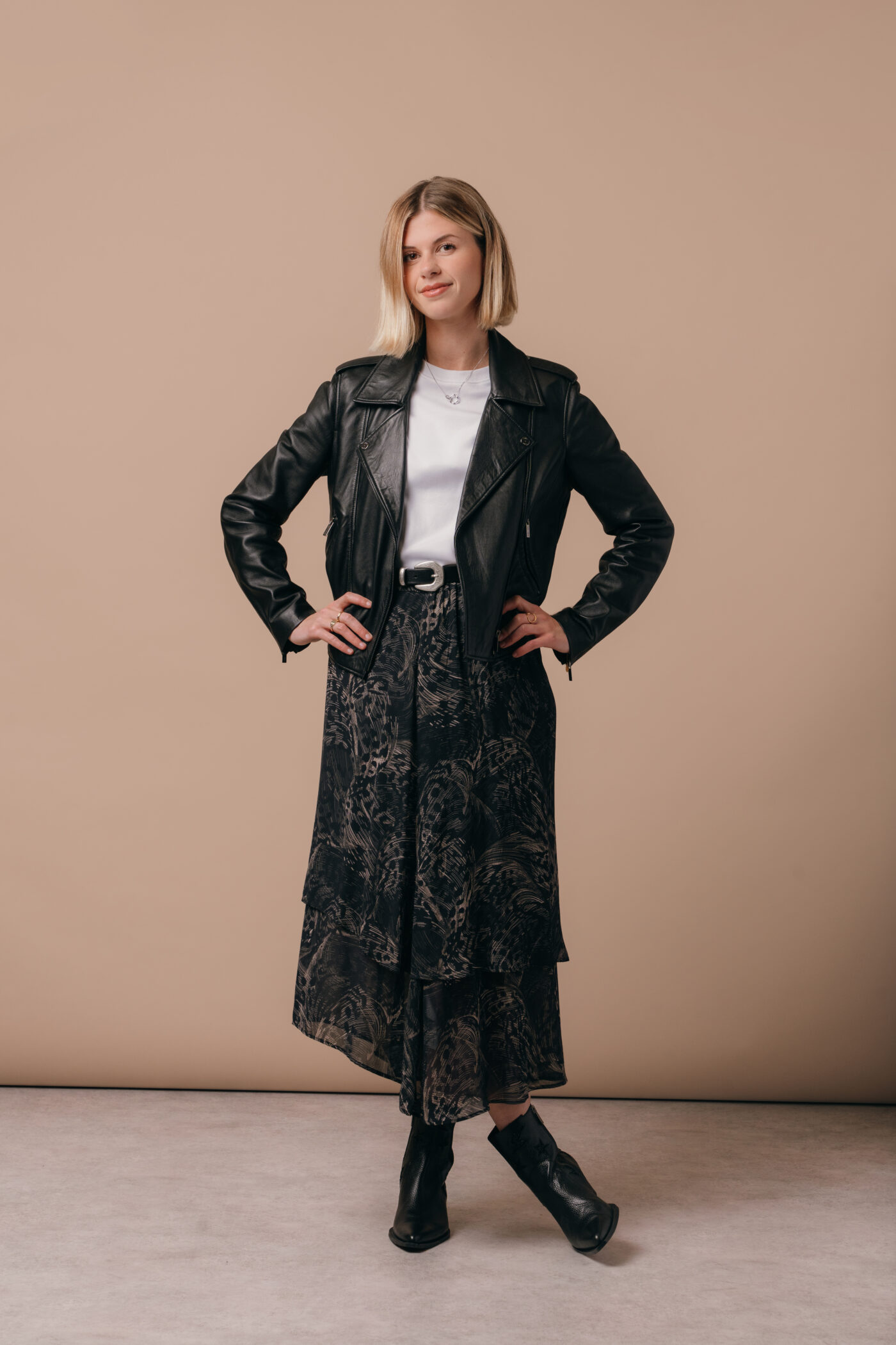 A model wearing a black Saint and Sofia leather jacket with a white tee and a feather print midi skirt.