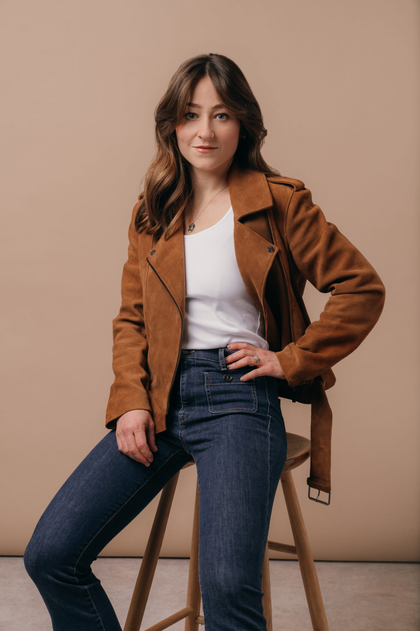 A model wearing a brown Saint and Sofia suede jacket with a white tank top, blue denim flared jeans