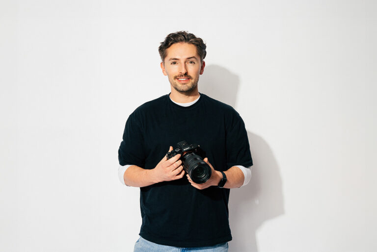 The Head of Creative at Saint and Sofia, Michael Higham, smiling at the camera while holding a camera in his hands