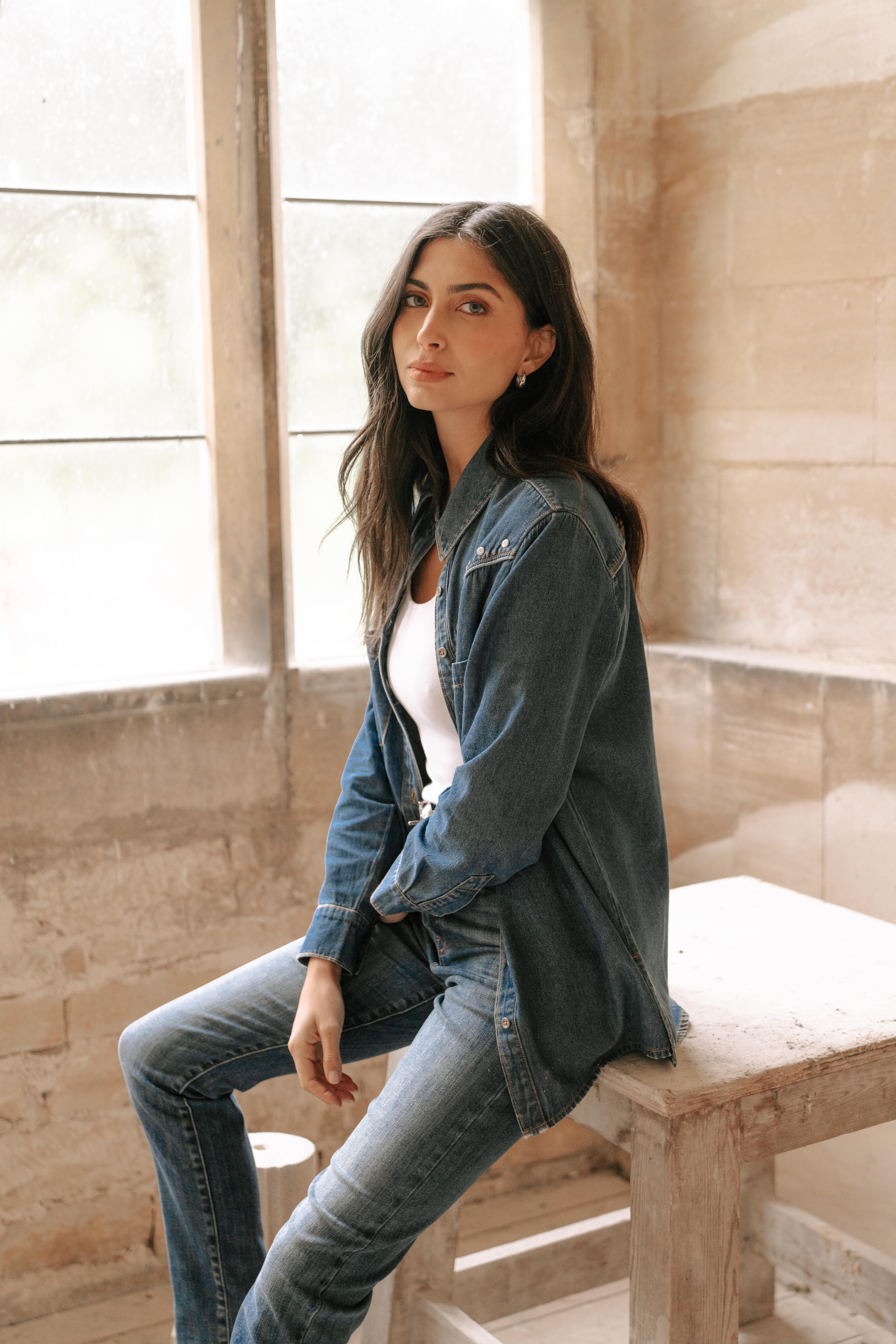 A model wearing the Sidney Denim Shirt with the Saint and Sofia Wide leg jeans for a double denim look. Worn over a white scoop neck vest.