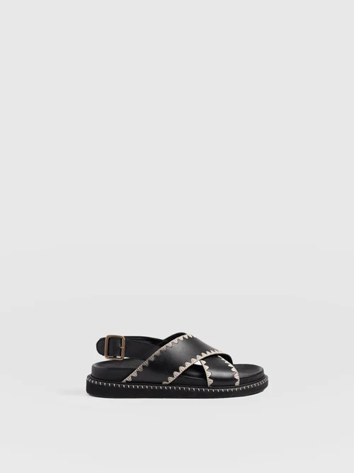 The Saint and Sofia Bonnie Cross Over Sandals. A black leather design with wide cross over straps and a buckled slingback. Raffia trims for extra detail.