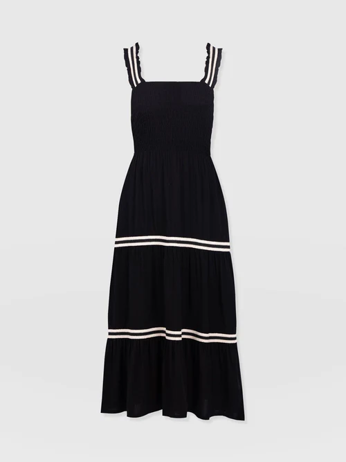 The Maya Shirring Dress by Saint and Sofia. A beautiful summer design in an easily wearable black with a sleeveless bodice, square neckline, and all over ruched effect. At the shirt, contrasting white stripes create a tiered effect.