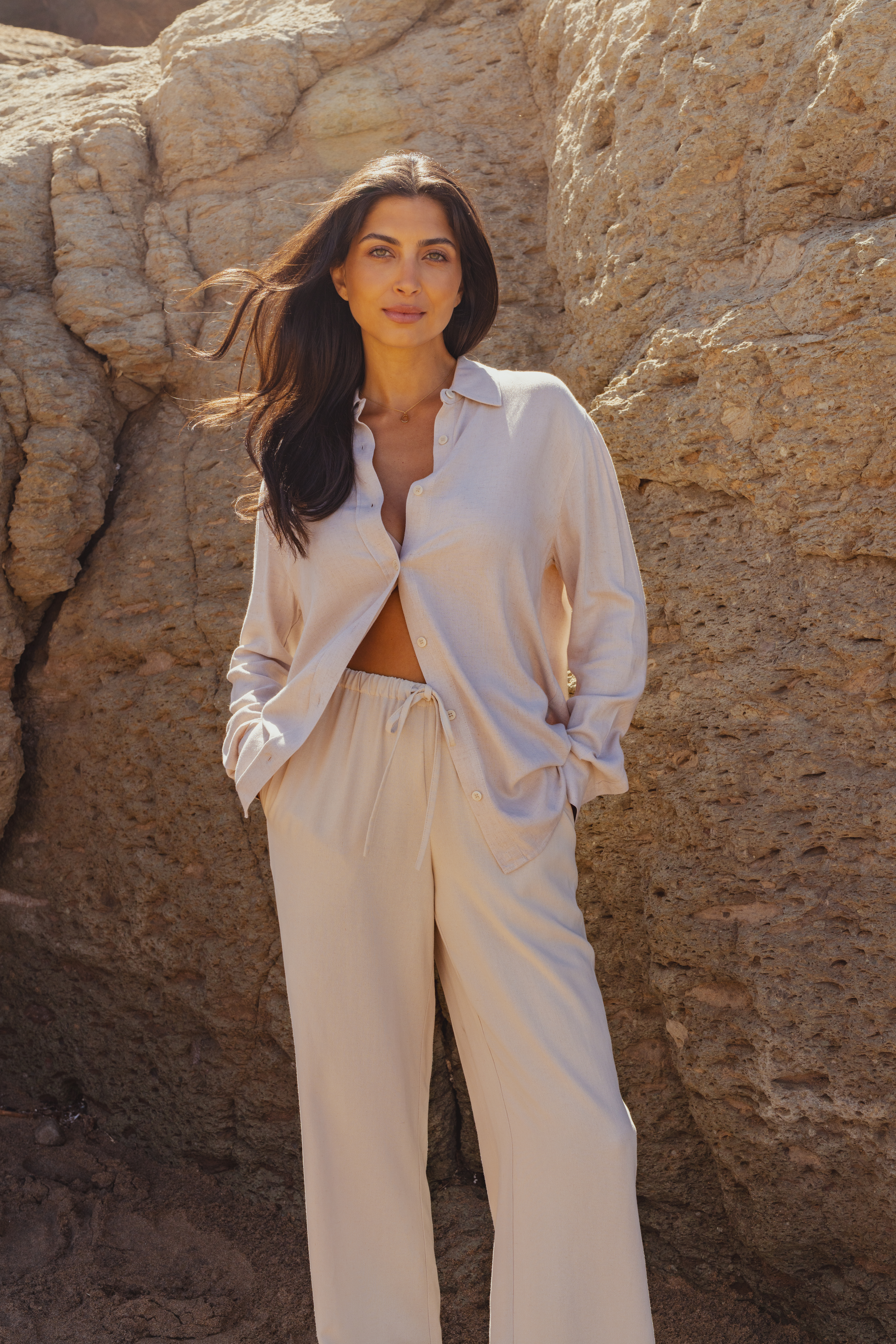 A model wearing a linen co-ord by Saint and Sofia. This boho style look features a cream button up shirt over a matching pair of wide leg linen trousers with a self tying waistband.