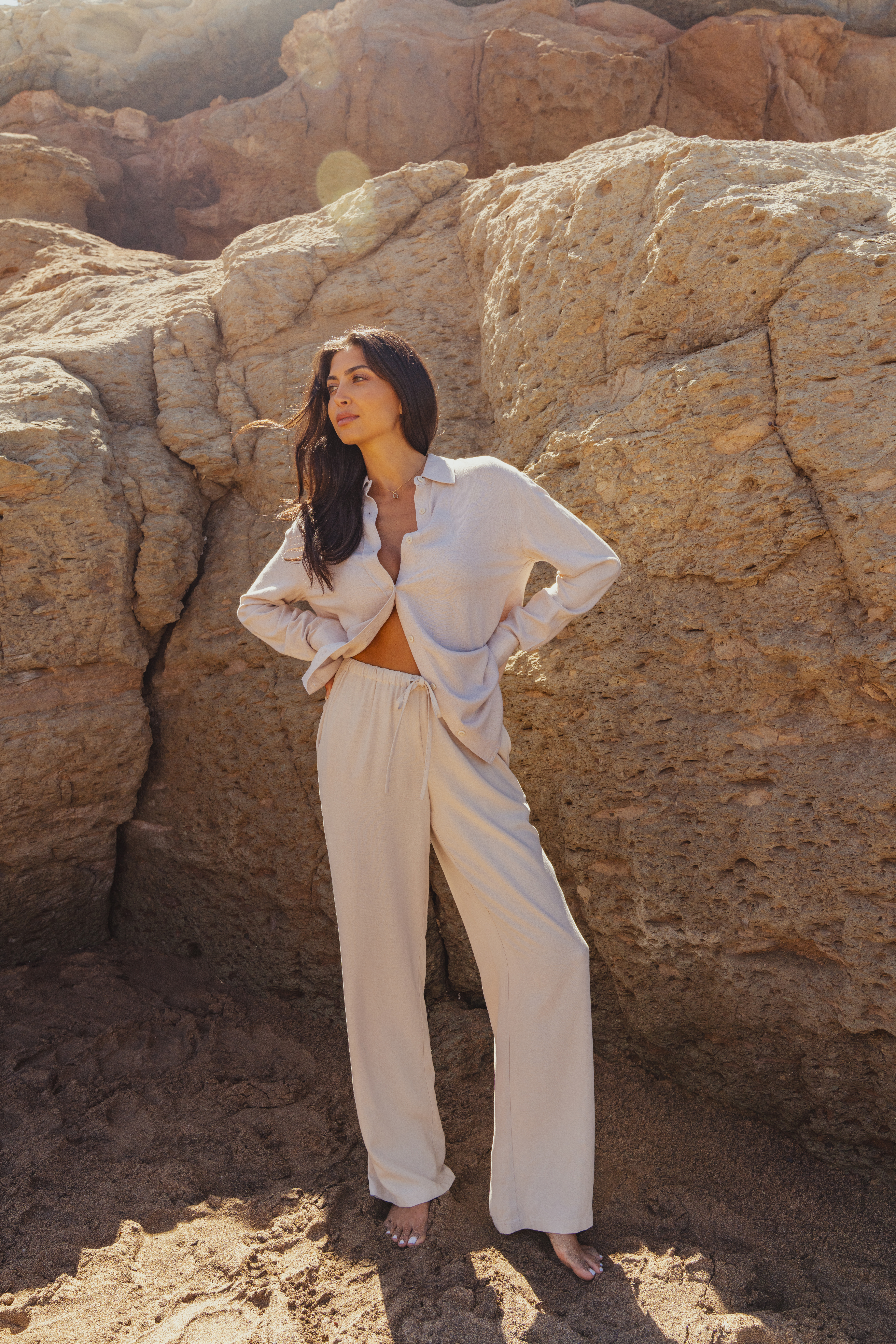 A model wearing a linen co-ord by Saint and Sofia. This boho style look features a cream button up shirt over a matching pair of wide leg linen trousers with a self tying waistband.