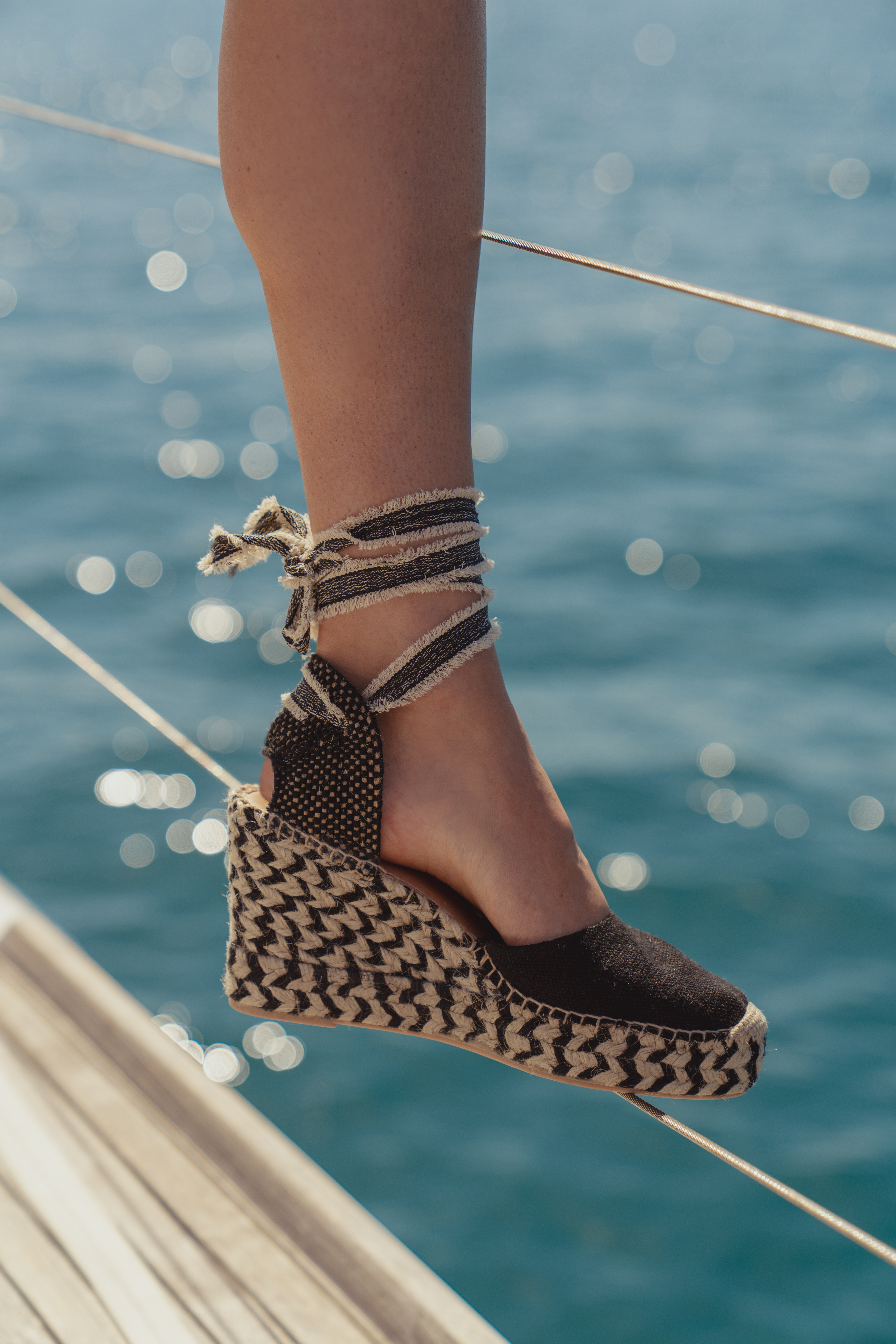 The Rowe Espadrille Wedges by Saint and Sofia. A black and beige design with a round toe and a wrap-around ankle strap that fastens in a bow at the back of the ankle. The perfect boho style to add to your footwear collection.
