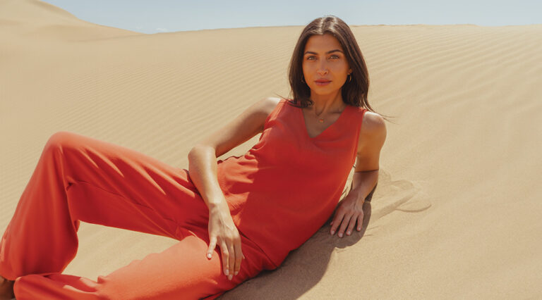 A model laying on the sand wearing a burnt orange linen co-ord by Saint and Sofia. A pair of wide leg trousers with a matching V-neck tunic top