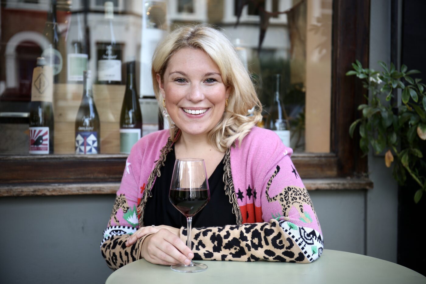 Founder of Laylo wine, Laura Riches sat on a table outside a bar, holding a glass of red wine and smiling at the camera.