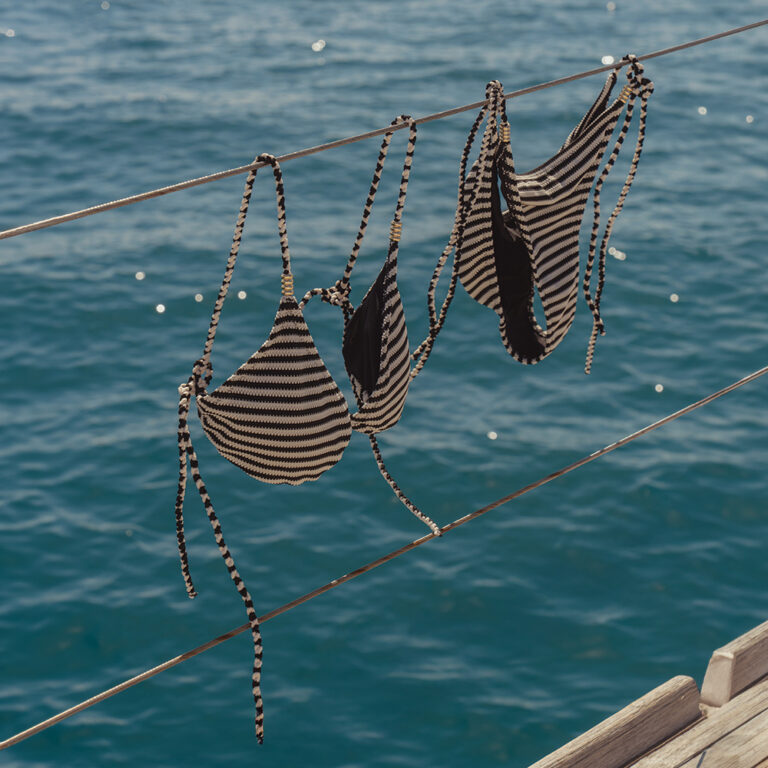 A striped bikini by saint and sofia hanging from the railings of a boat with the ocean as the backdrop