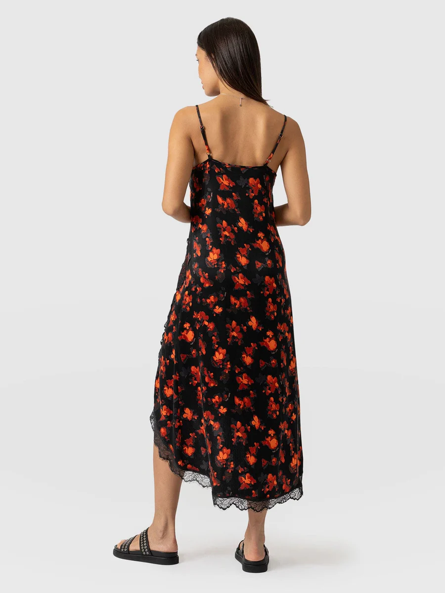 A model wearing the Saint and Sofia Harper Lace Cami Dress. A red and black wedding guest dress with lace trims and an asymmetric hemline.