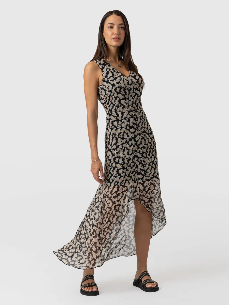 A model wearing the Saint and Sofia Lexi High Low Dress. A blurred floral design with an asymmetric hem and a V neckline. The perfect wedding guest dress.