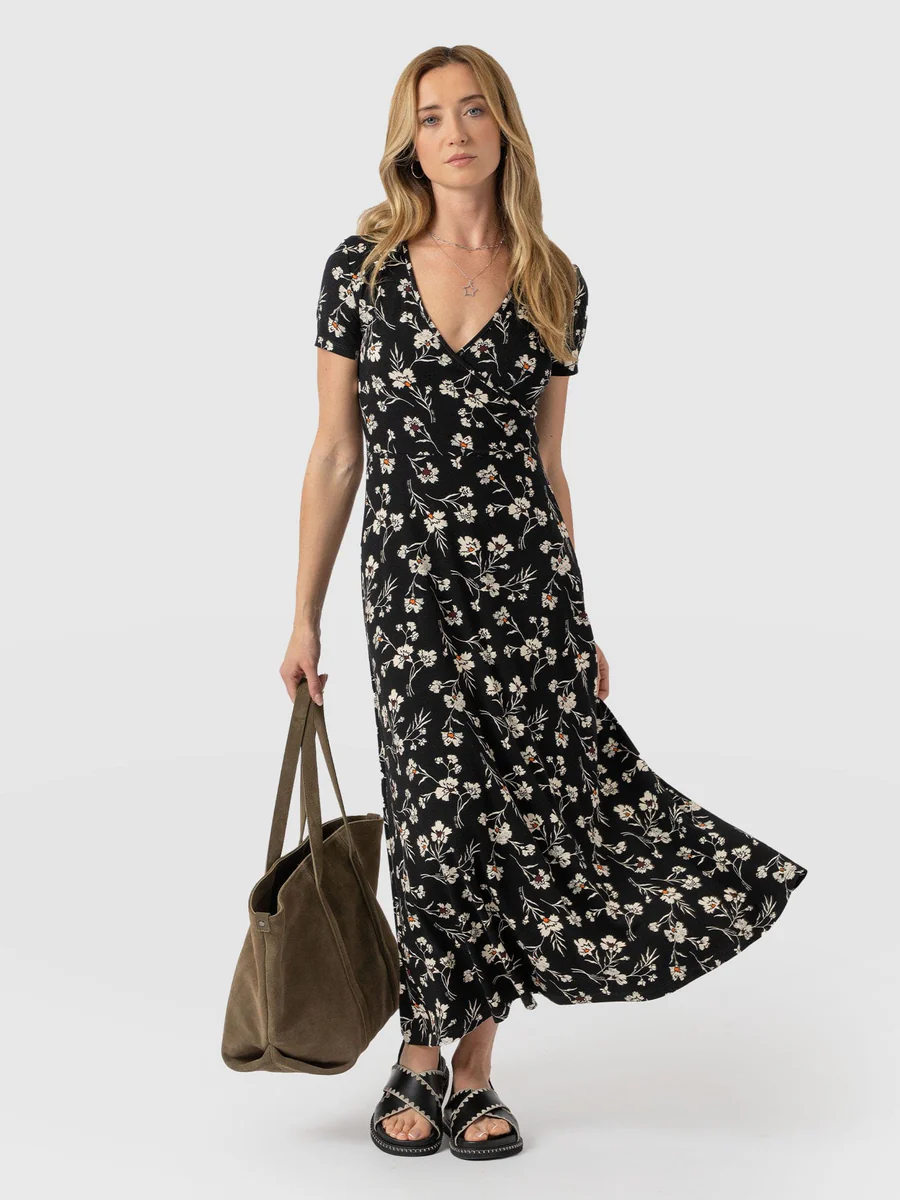 A model wearing the Saint and Sofia Maggie Wrap Dress with short sleeves. A floral wedding guest dress with a V neckline and midi length skirt.