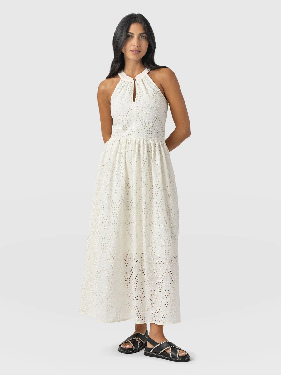 A model wearing the Saint and Sofia Zoey Halter Neck Dress. A white midi length design with broderie anglaise and a cut out at the neckline. The perfect summer evening dress.