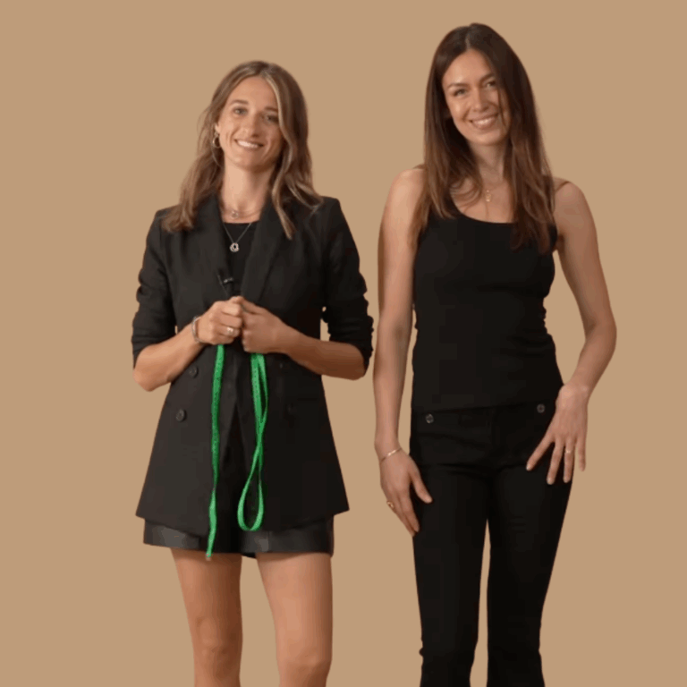 Two models standing in front of a brown background wearing all black. One holds a tape measure ready to measure the body shape of the other model.