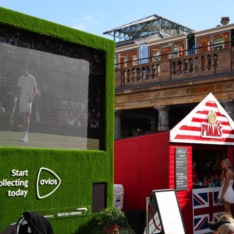 The Wimbledon Big Screen in Covent Garden Piazza with the pop up Pimm's bar in a red and white striped beach hut to the right.