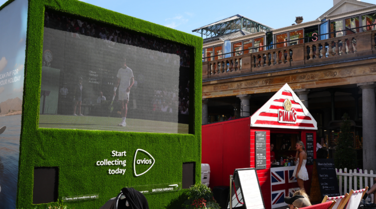 The Wimbledon Big Screen in Covent Garden Piazza with the pop up Pimm's bar in a red and white striped beach hut to the right.