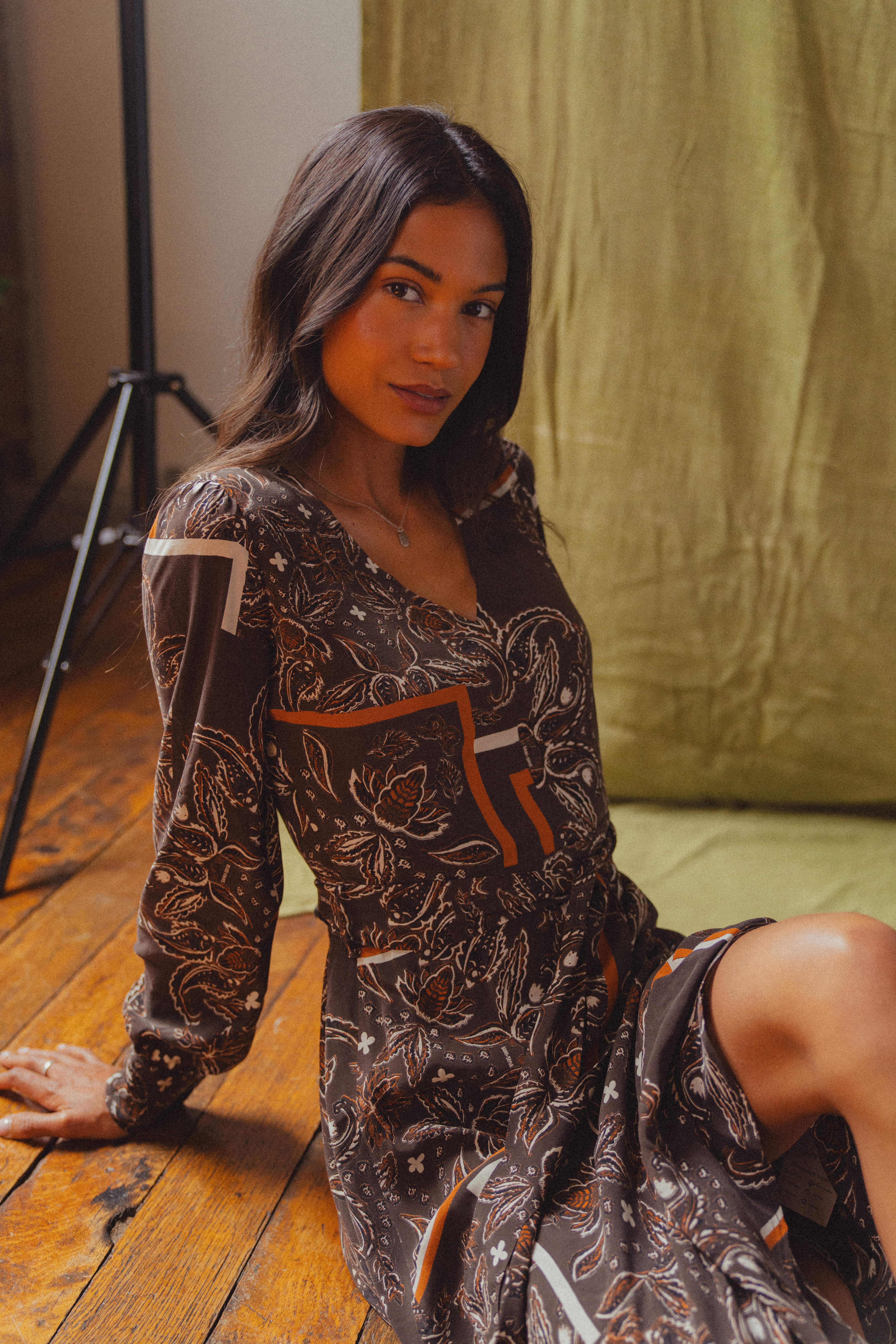 A model sat on the floor wearing the Saint + Sofia Naya V Neck Dress in brown paisley.