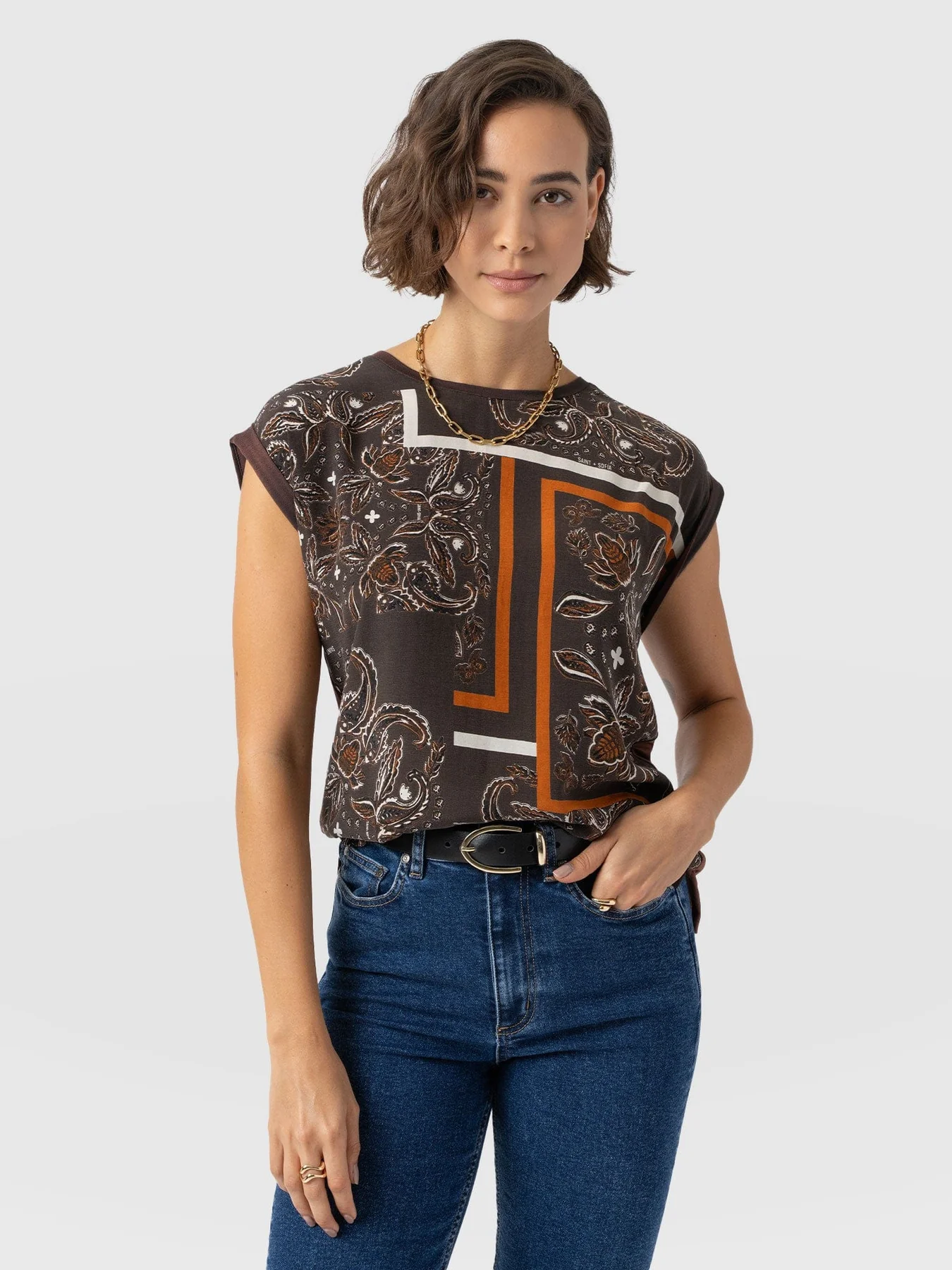 A model standing in front of a white backdrop wearing the Saint + Sofia Turn Up Contrast tee with a brown paisley pattern at the front and a contrasting solid colour back