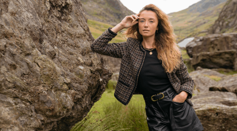 A model standing in a nature reserve wearing the new Saint + Sofia boucle jacket, a black tee, and a pair of leather leather shorts
