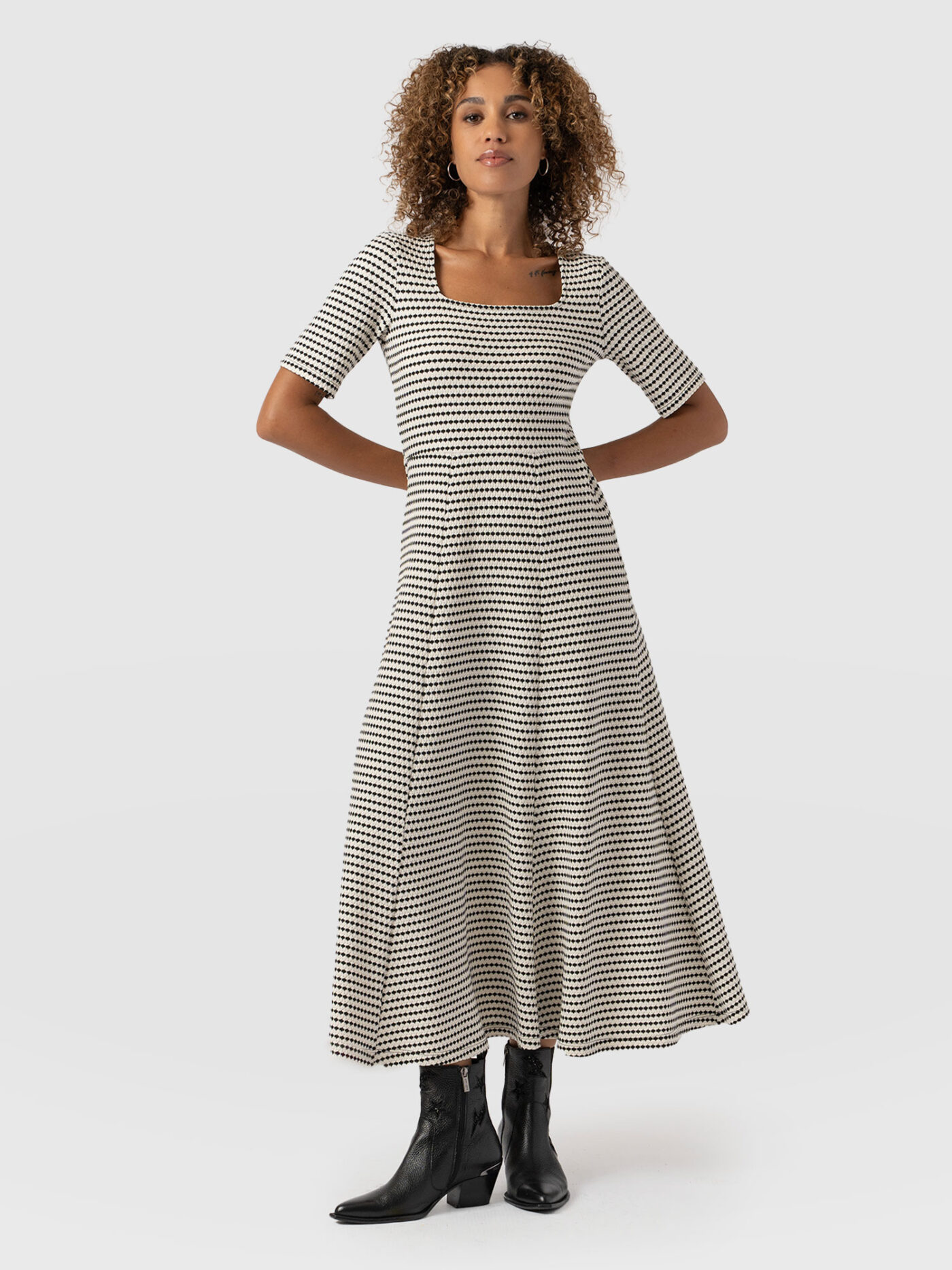 A model wearing the Saint and Sofia Darcey Flared Dress. It's handmade from a black and white textured material and features a square neckline, short sleeves, and an Empire Waist that falls into a full skirt for a sculpted figure.