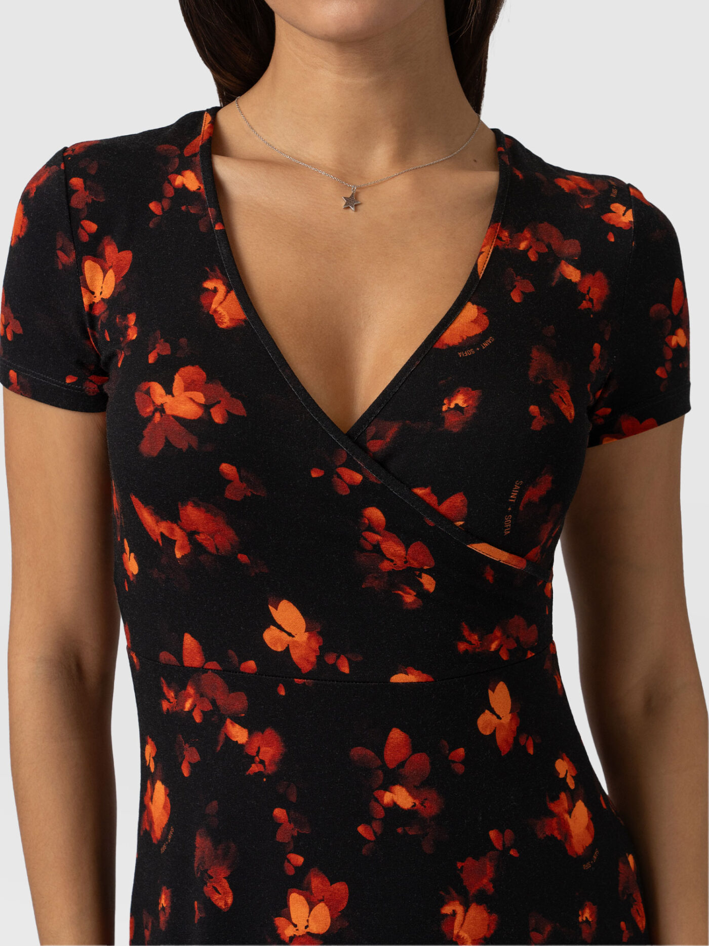 A close up picture of the Saint and Sofia Maggie Wrap Dress. This design is shaped with a mock wrap bodice that meets in a V neckline. This print features a black background with red flowers.