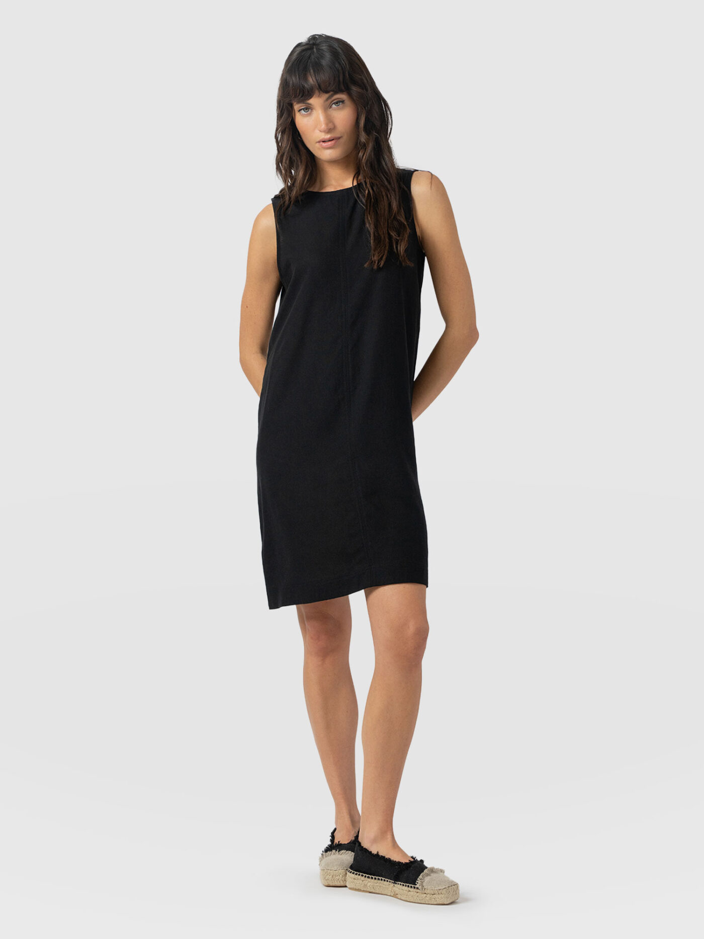 A model wearing the Saint and Sofia Corinne Shift Dress in black. A crew neck, sleeveless mini that falls loosely over your figure and is perfect for appl body shapes.