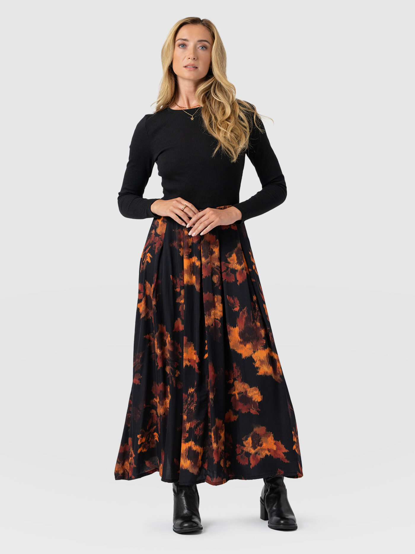 A model wearing the Saint and Sofia Renee Contrast Dress. A long sleeve design with a fitted bodice and a full, pleated skirt for a fit-and-flare silhouette. Here, the model wears it with a pair of leather boots.