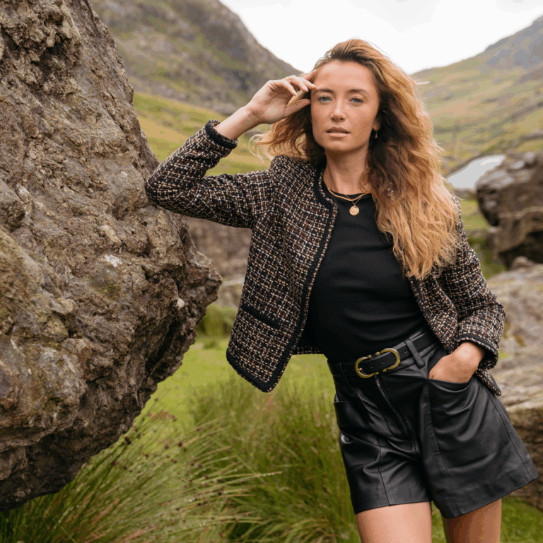 A model standing in a nature reserve wearing the new Saint + Sofia boucle jacket, a black tee, and a pair of leather leather shorts