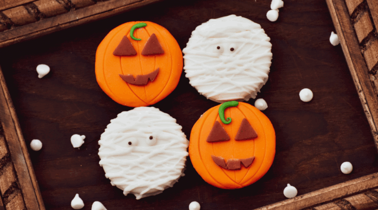 A tray of four halloween cookies. Two are iced with a pumpkin design and two are iced with a Mummy design.