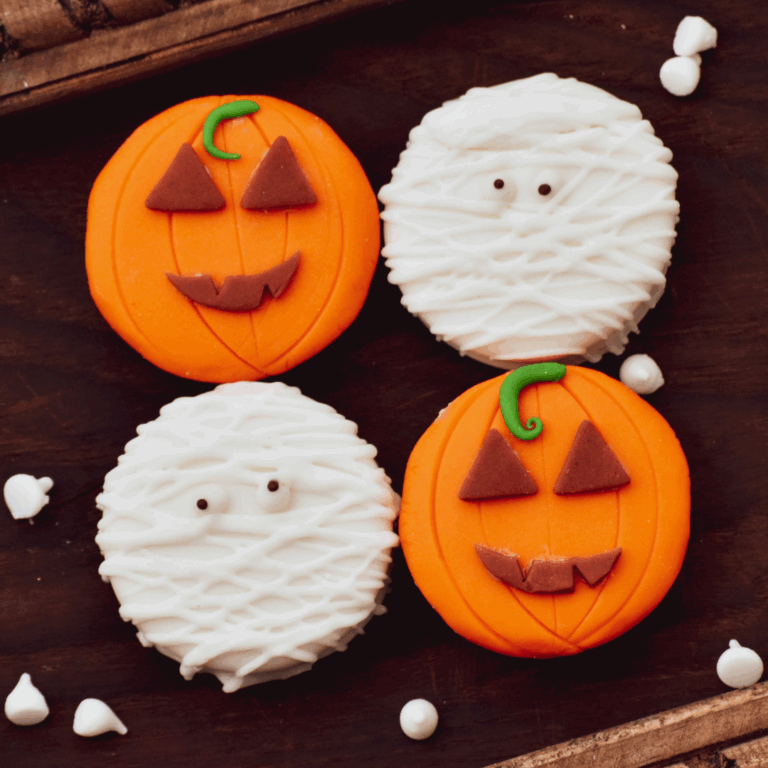 A tray of four halloween cookies. Two are iced with a pumpkin design and two are iced with a Mummy design.