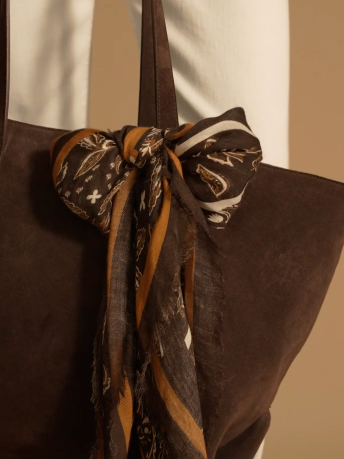 A close up shot of the Kara bag by Saint and Sofia with the brown paisley Wren scarf tied in a bow around the handle as a bag scarf.