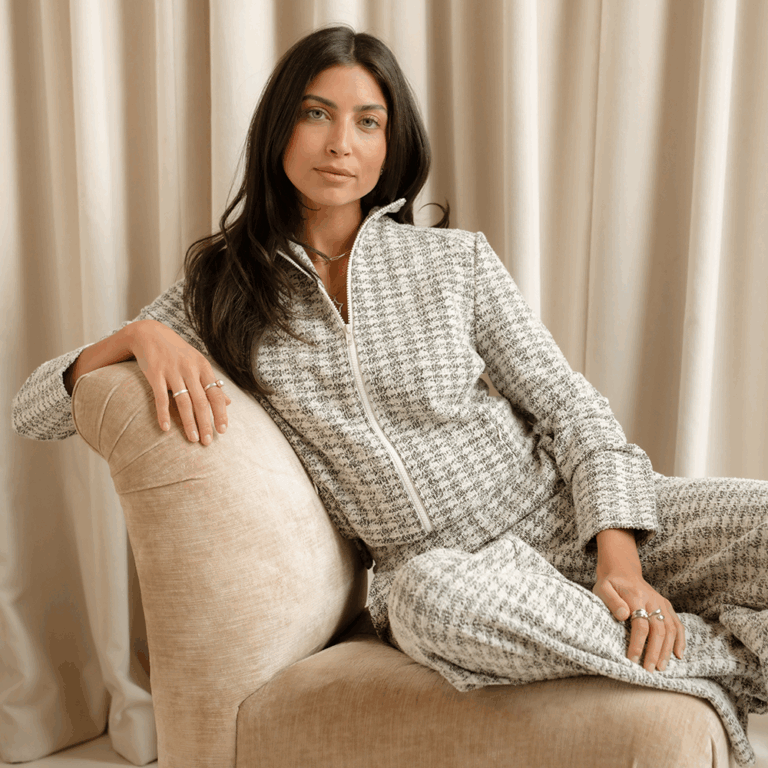 A model lounging on a cream sofa in front of a cream curtain back drop wearing the new Saint + Sofia grey and white boucle loungewear set.