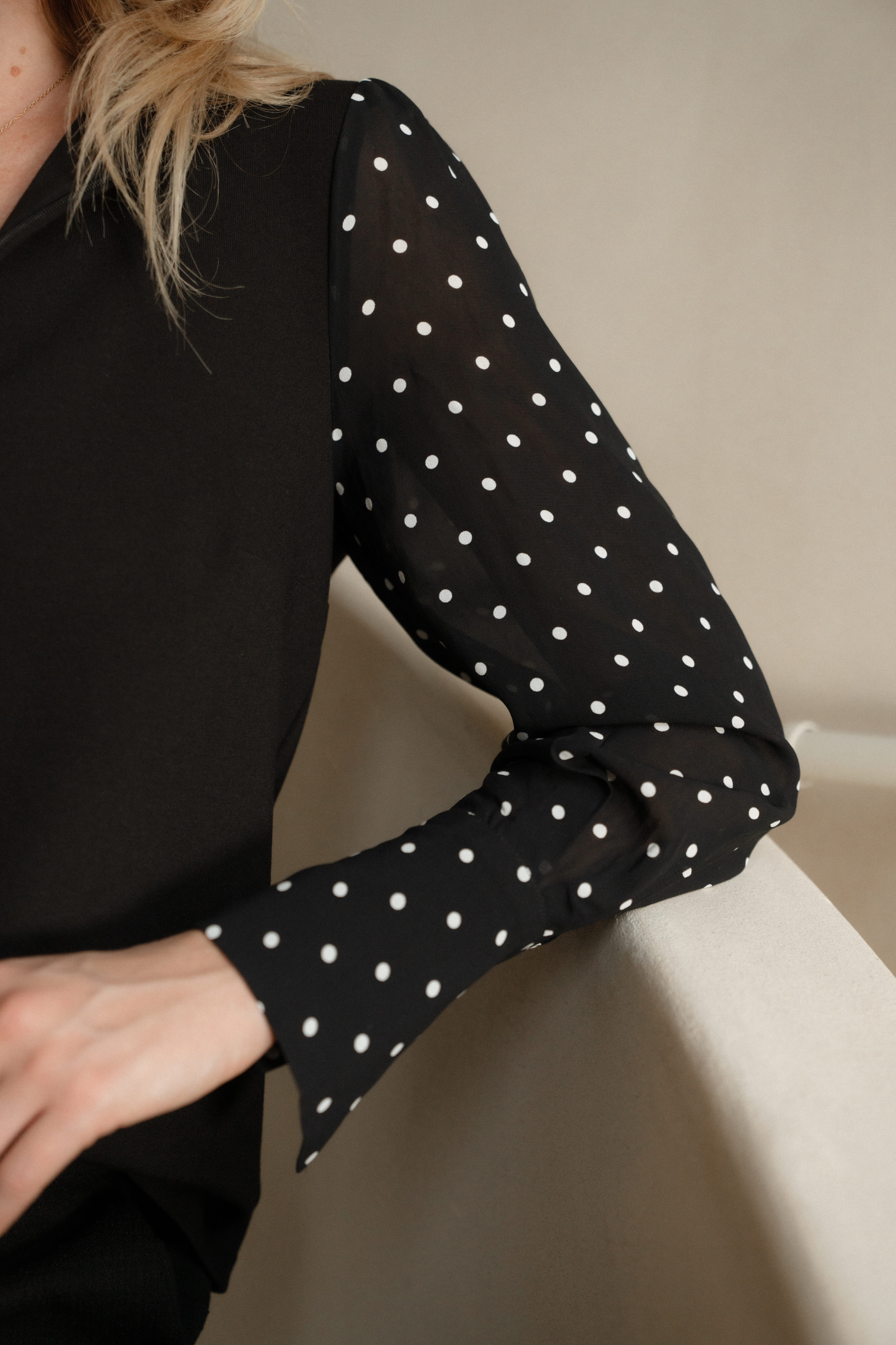A model's bent arm as it leans on the a staircases banister wearing a black blouse with black and white polka dot bishop sleeves.