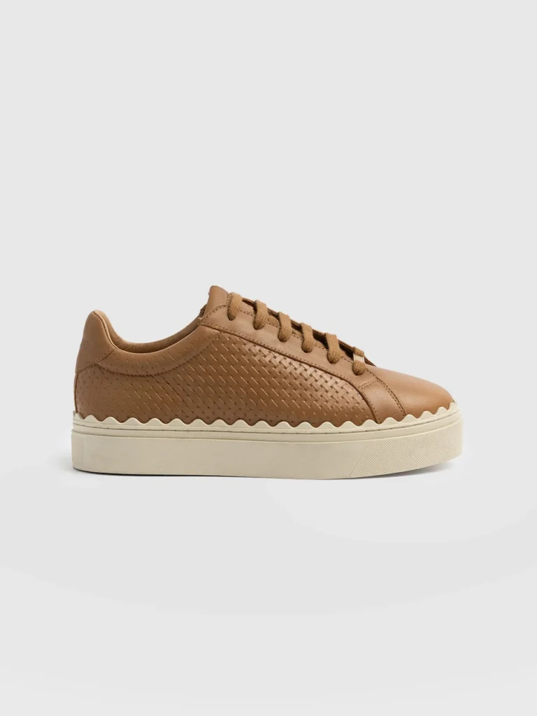 A pair of brown leather trainers with a scalloped trim sole.