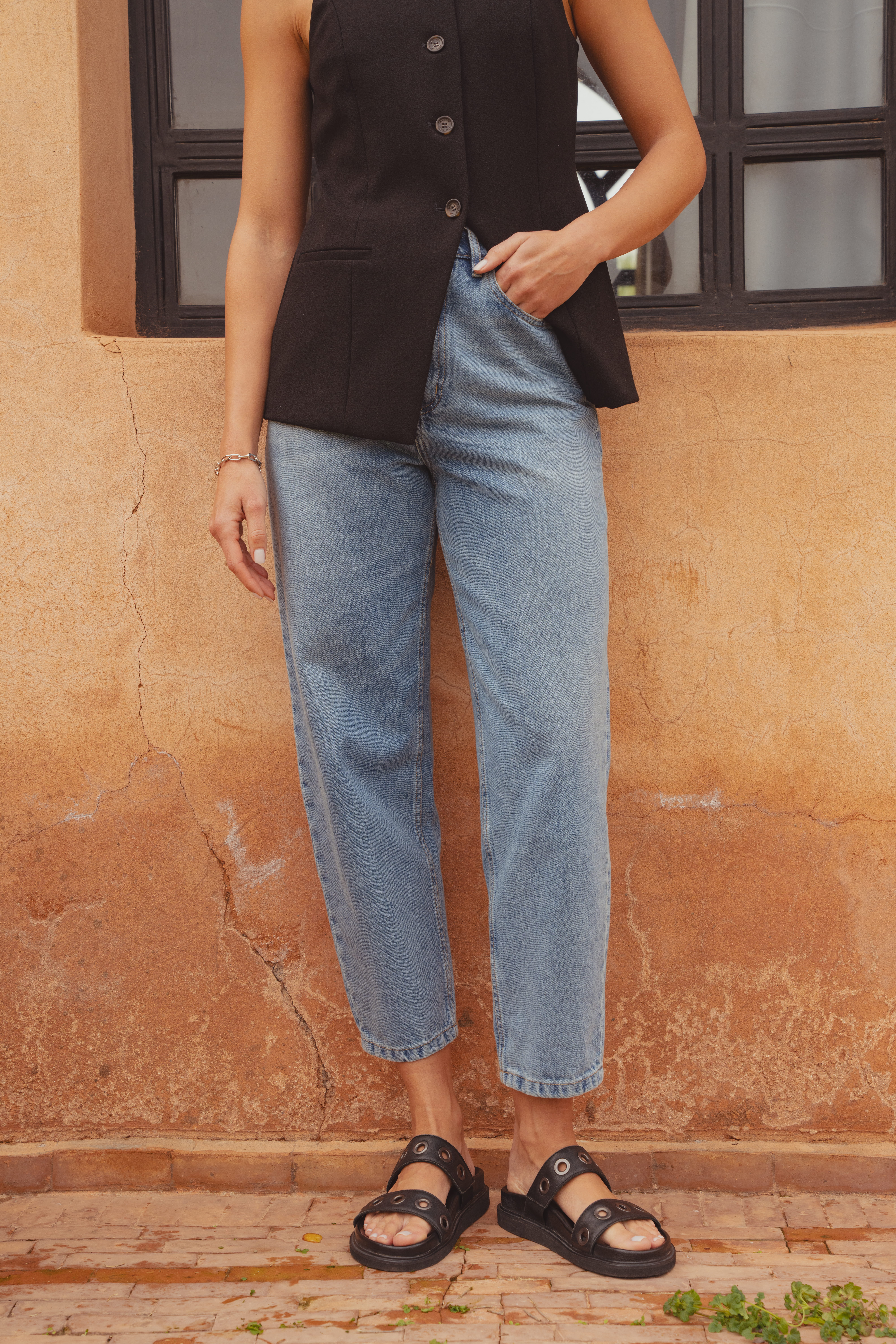 A close-up shot of the Saint and Sofia mid blue barrel leg jeans. Their rounded shape cuts just above the ankle to make a show of the shoes which are leather eyelet sliders.