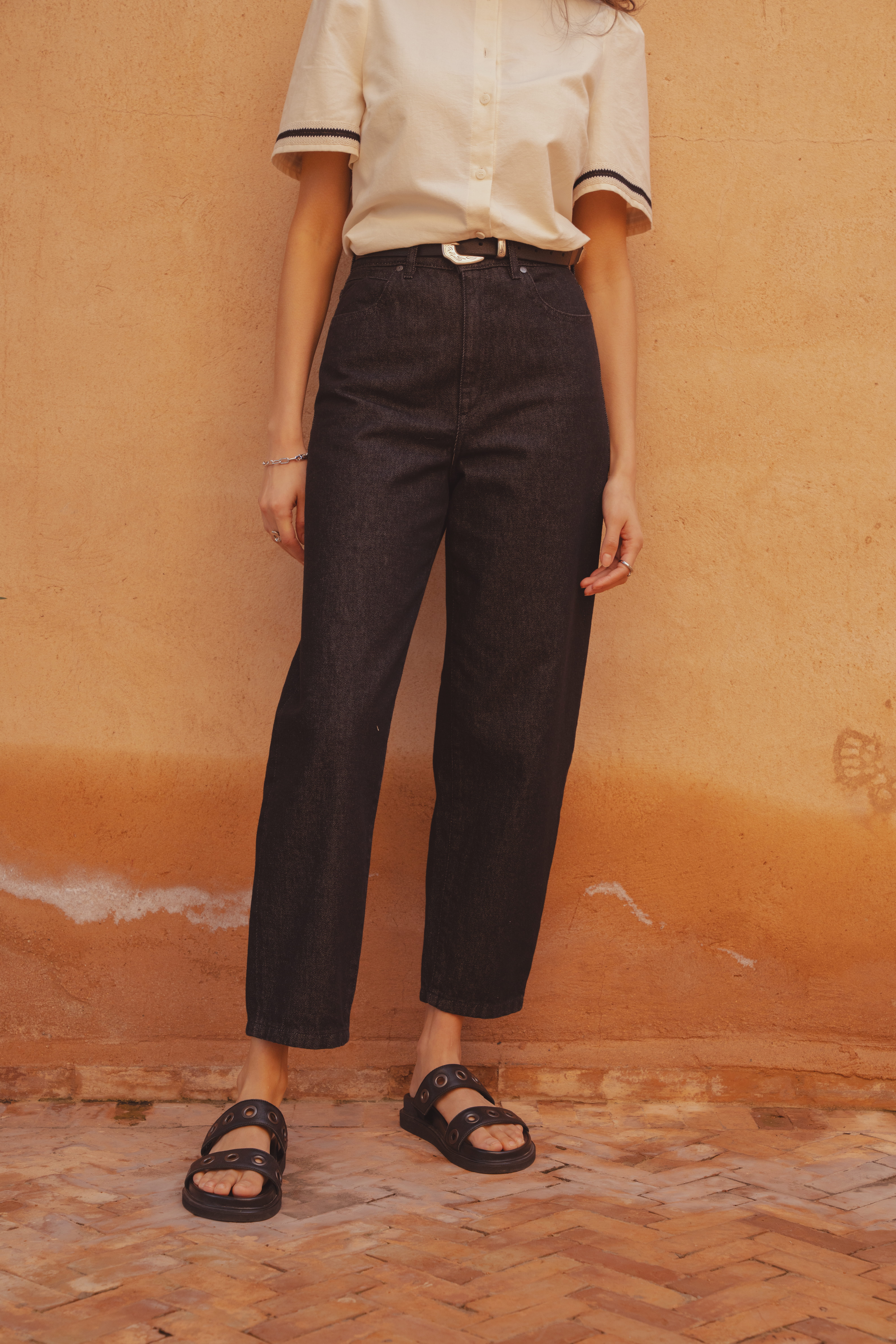 A close up shot of the Saint and Sofia black barrel leg jeans which hold a rounded shape and cut just above the ankle for an ankle-grazing look. They're styled hear with leather sliders.