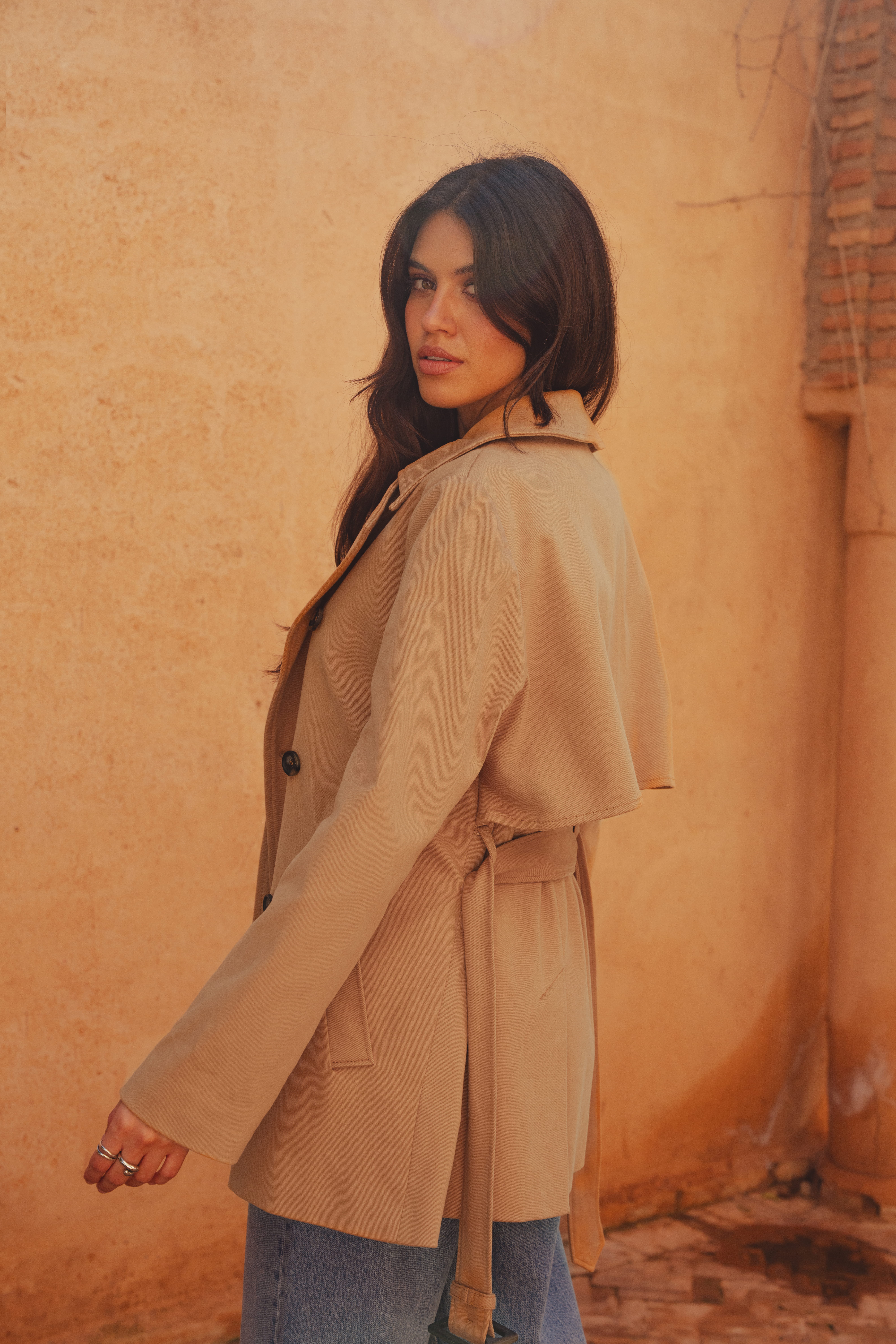 A model with her back to the camera showing the Marion Short Trench from Saint and Sofia and its rain guard at the back and belted waist.