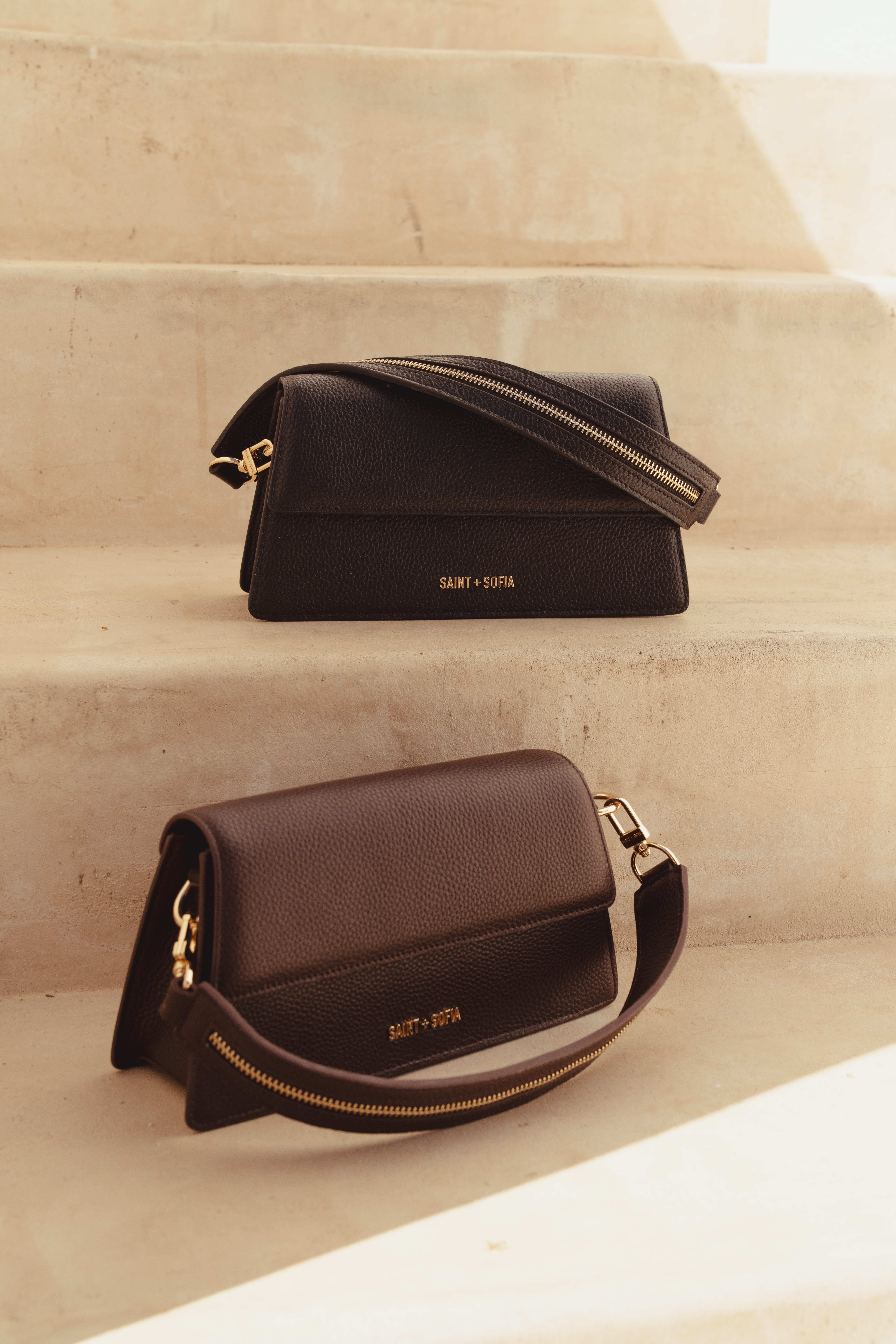 The two Lennox Half Flap Bags from Saint and Sofia. Miniature shoulder bag styles made from grained leather. The black and brown iterations are photographed here separate steps.