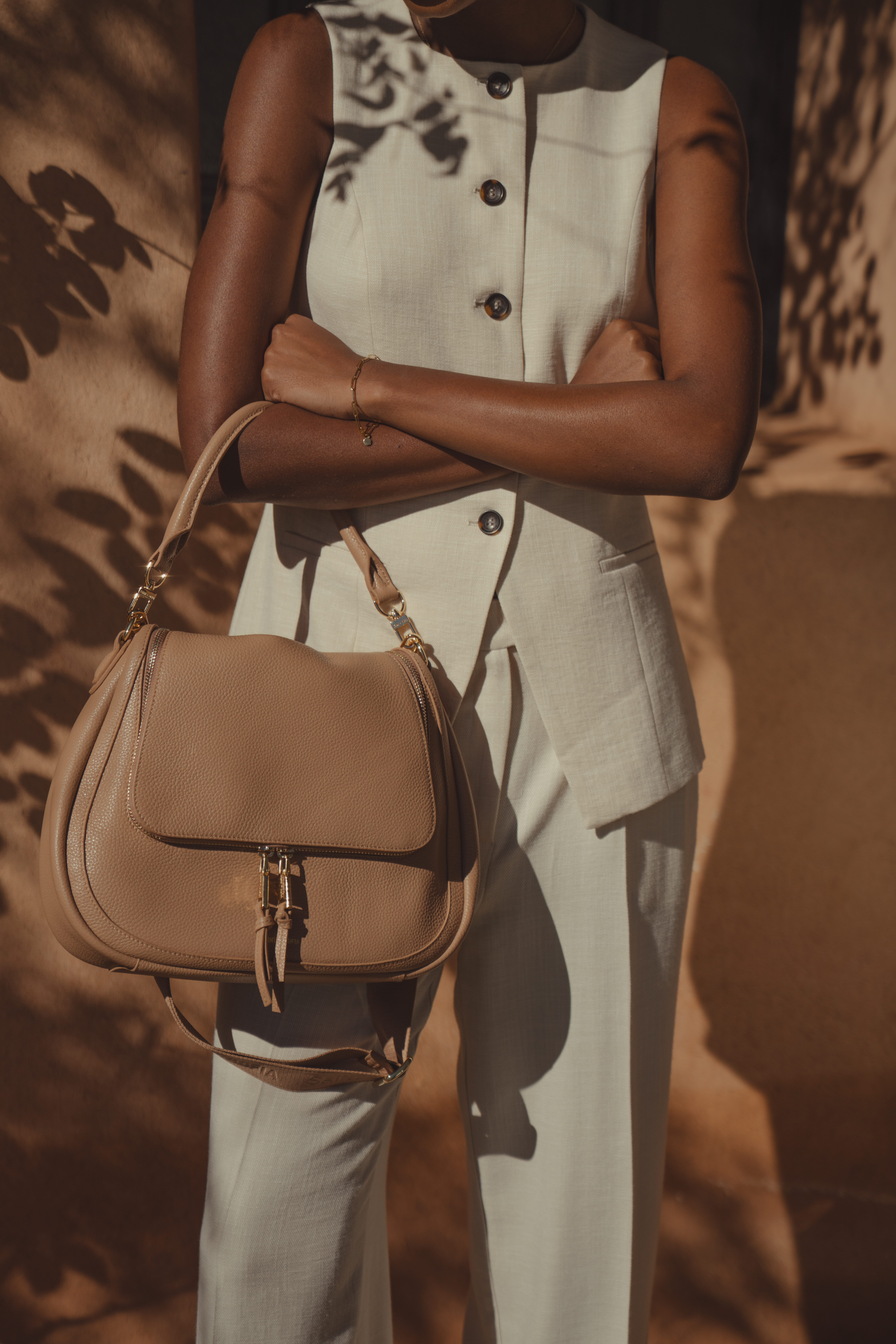 A close up shot of a model wearing at the oatmeal waistcoat and trouser set by Saint and Sofia. A longline design with horn button fastening down the front. Worn here with wide leg trousers and the Marlowe Messenger Bag in Caramel by Saint and Sofia.
