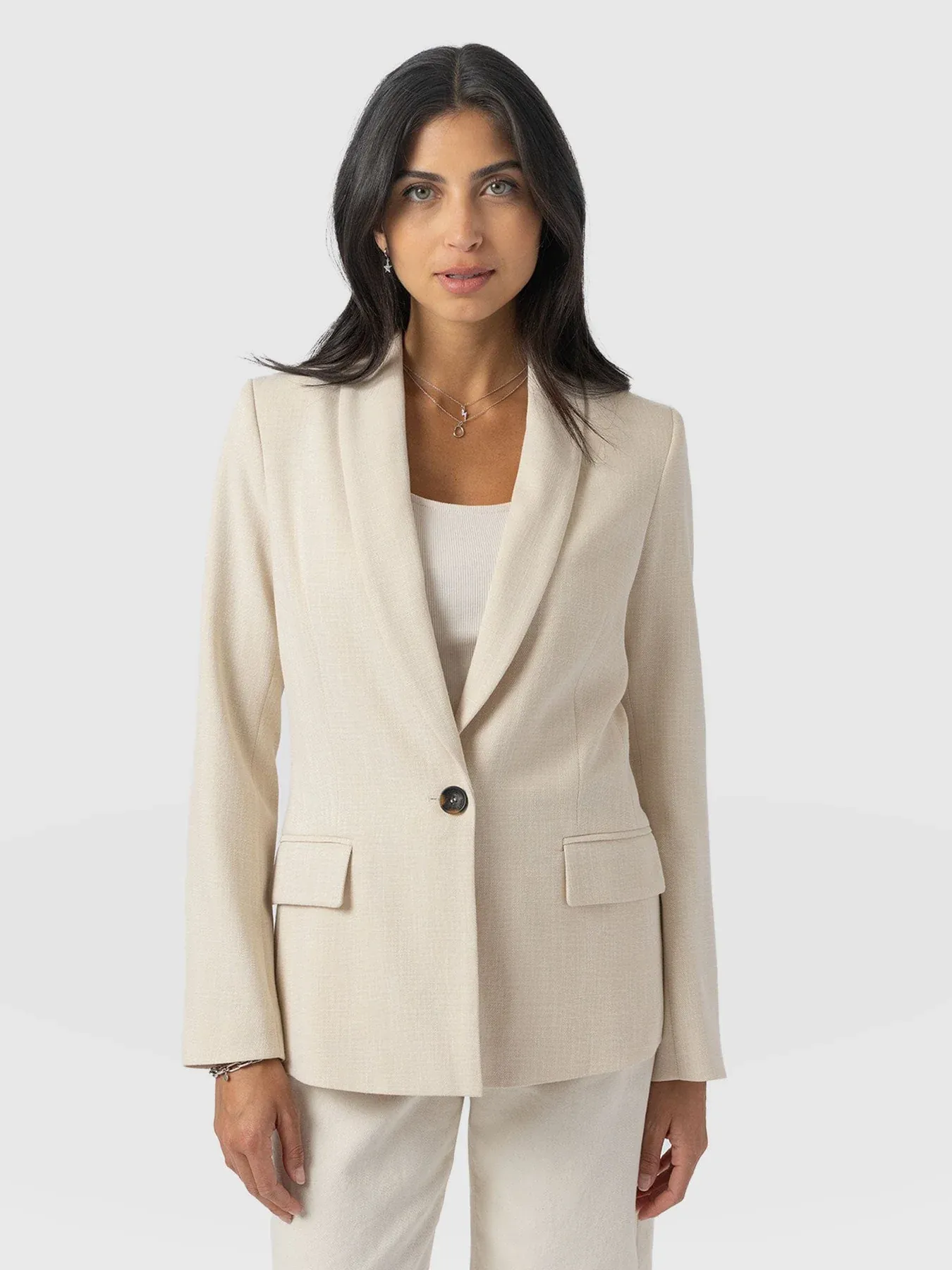 A model wearing a cream blazer from Saint and Sofia. The Argent Blazer is a single breasted design with a shawl collar. It's styled here with the matching cream trousers.