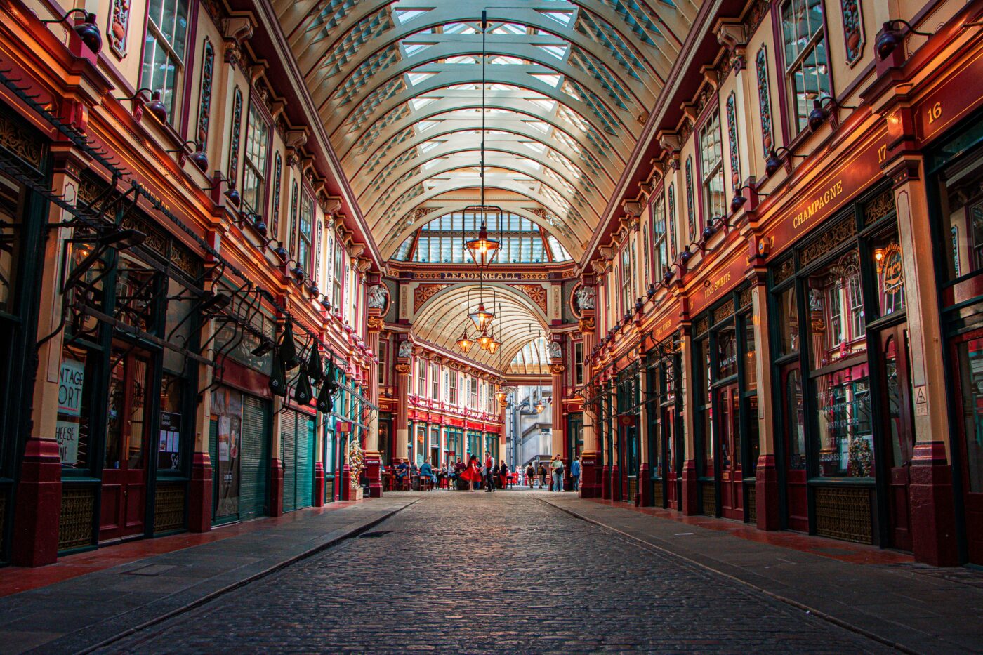 A low down picture of Leadenhall Market. The cobbled street is clear. In the distance people mingle around tables outside a restaurant.