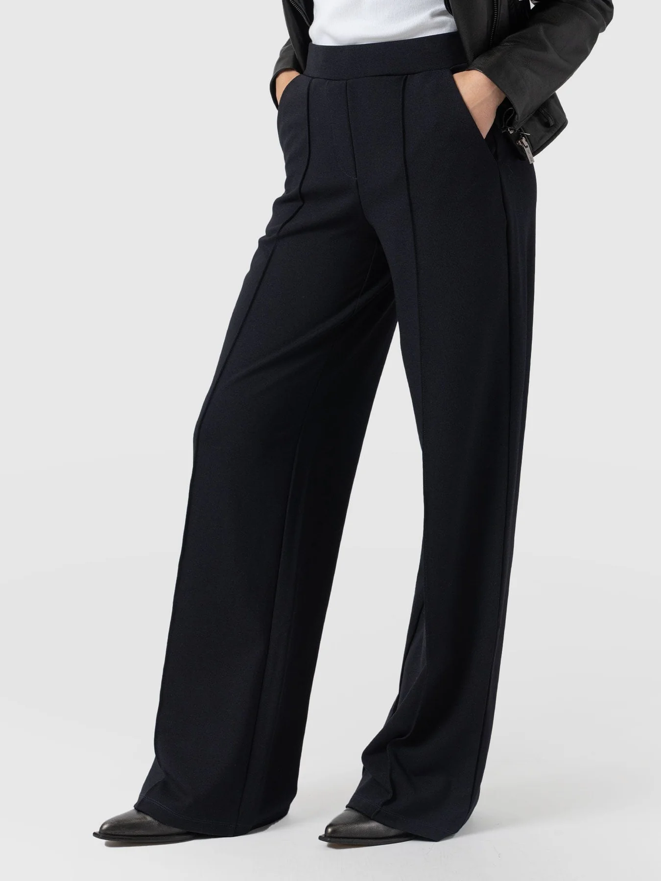 A close up shot of the Keller Pant by Saint and Sofia, a wide leg trouser with a front pin tuck detail and flat waistband. Styled here with pointed toe leather boots.